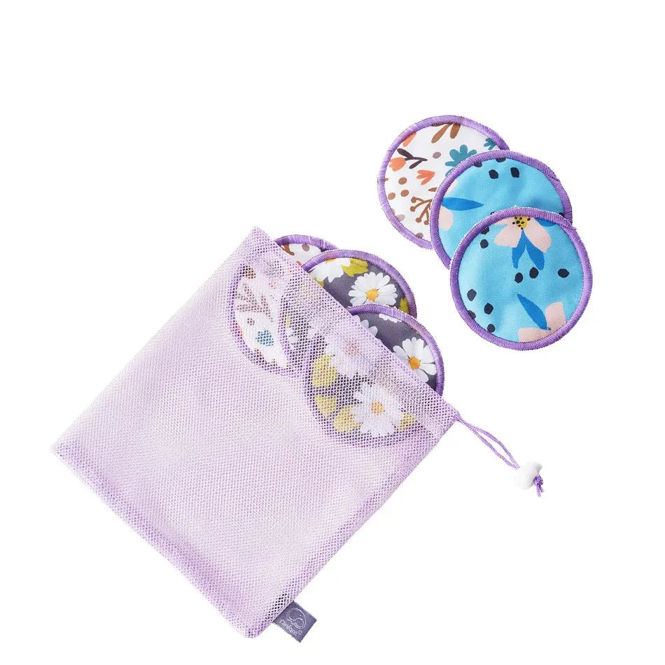 A lavender mesh drawstring bag containing reusable cloth pads, with three circular pads displayed outside the bag on a white background. The pads have floral and abstract prints in blue, purple, white, and yellow.