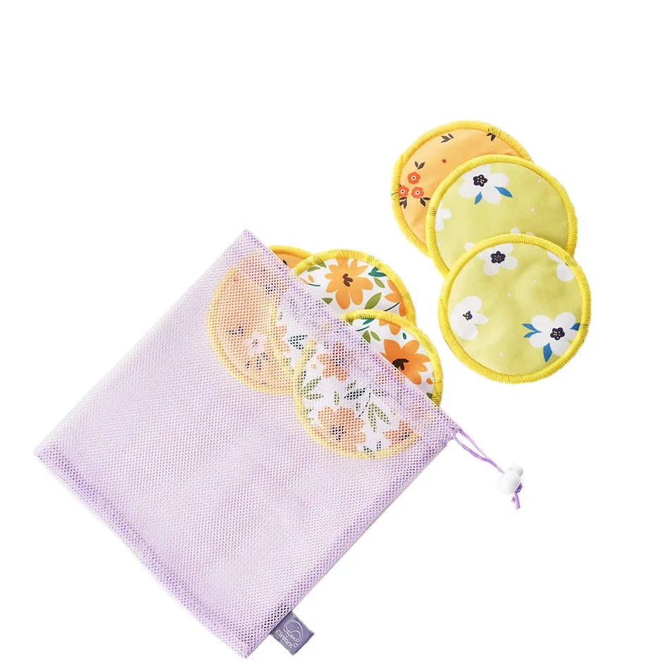 A set of reusable cotton breast pump or nursing pads with floral prints in yellow, orange, and white, shown alongside a lavender mesh storage bag on a white background. A purple label at the top displays the letter 'B'.
