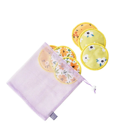 A set of reusable cotton breast pump or nursing pads with floral prints in yellow, orange, and white, shown alongside a lavender mesh storage bag on a white background. A purple label at the top displays the letter 'B'.