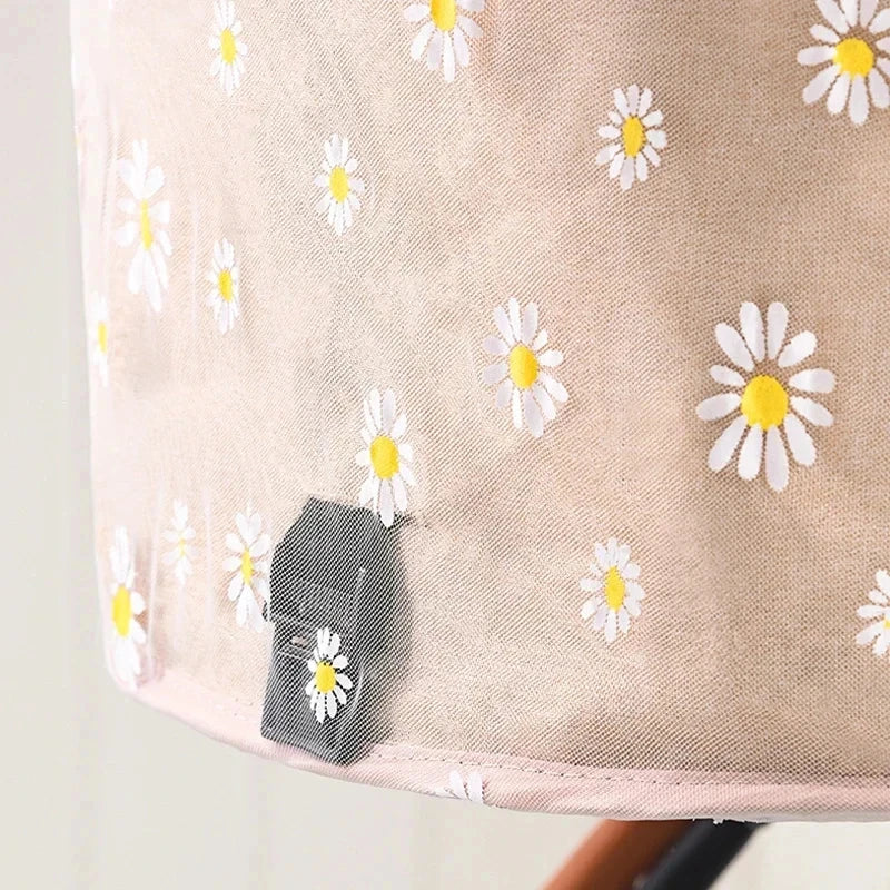 Beige fabric with white daisy flowers and a small black hexagonal object on a light gray background