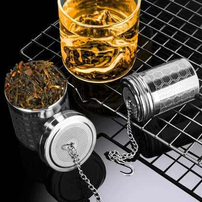 Tea infuser with loose tea leaves and a glass of tea on a black metal grid.